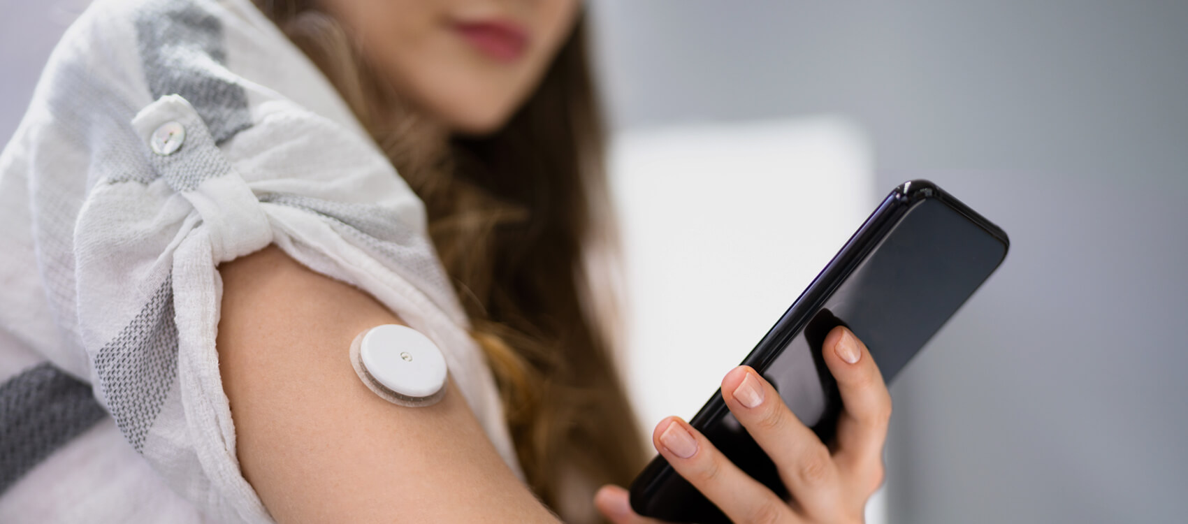 a woman with a digital diabetes monitor on her arm using a mobile app to measure her blood sugar levels
