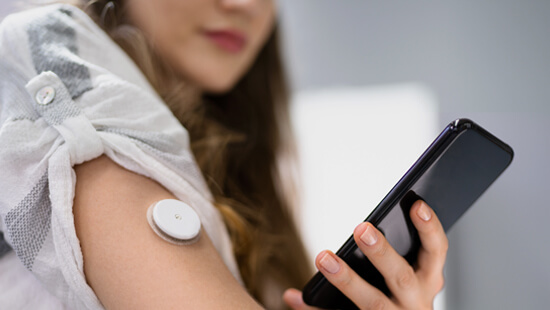 a woman with a digital diabetes monitor on her arm using a mobile app to measure her blood sugar levels