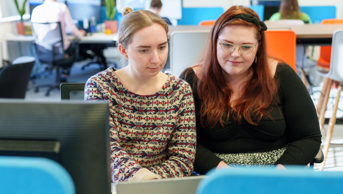 two coworkers sharing a laptop together whilst looking at the screen