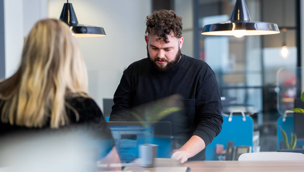 two coworkers sitting at a meeting table troubleshooting an issue on their laptops