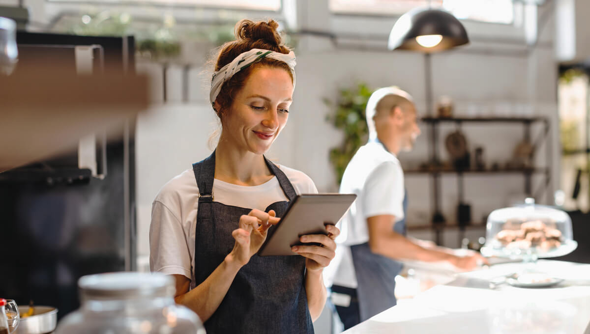 a cafe owner smiling whilst using her tablet at the food counter