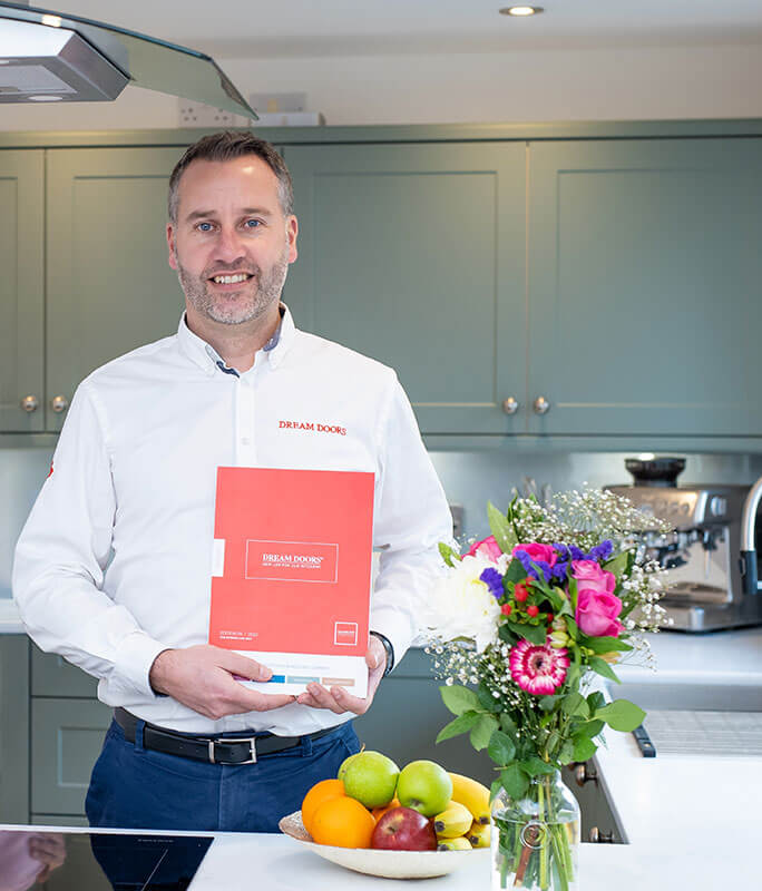 a man standing proudly in a modern kitchen holding a bright red brochure