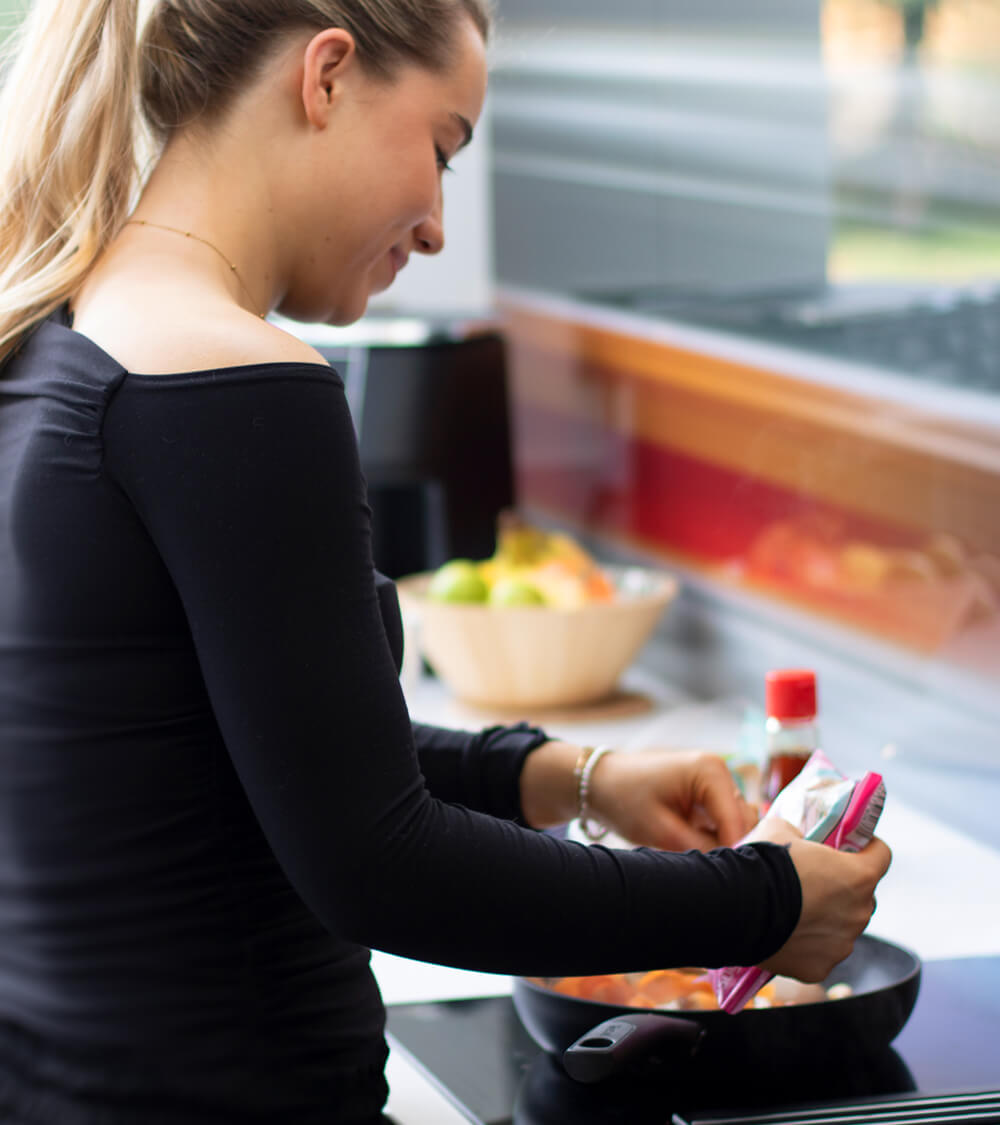 a student cooking noodles in a wok on their kitchen hob