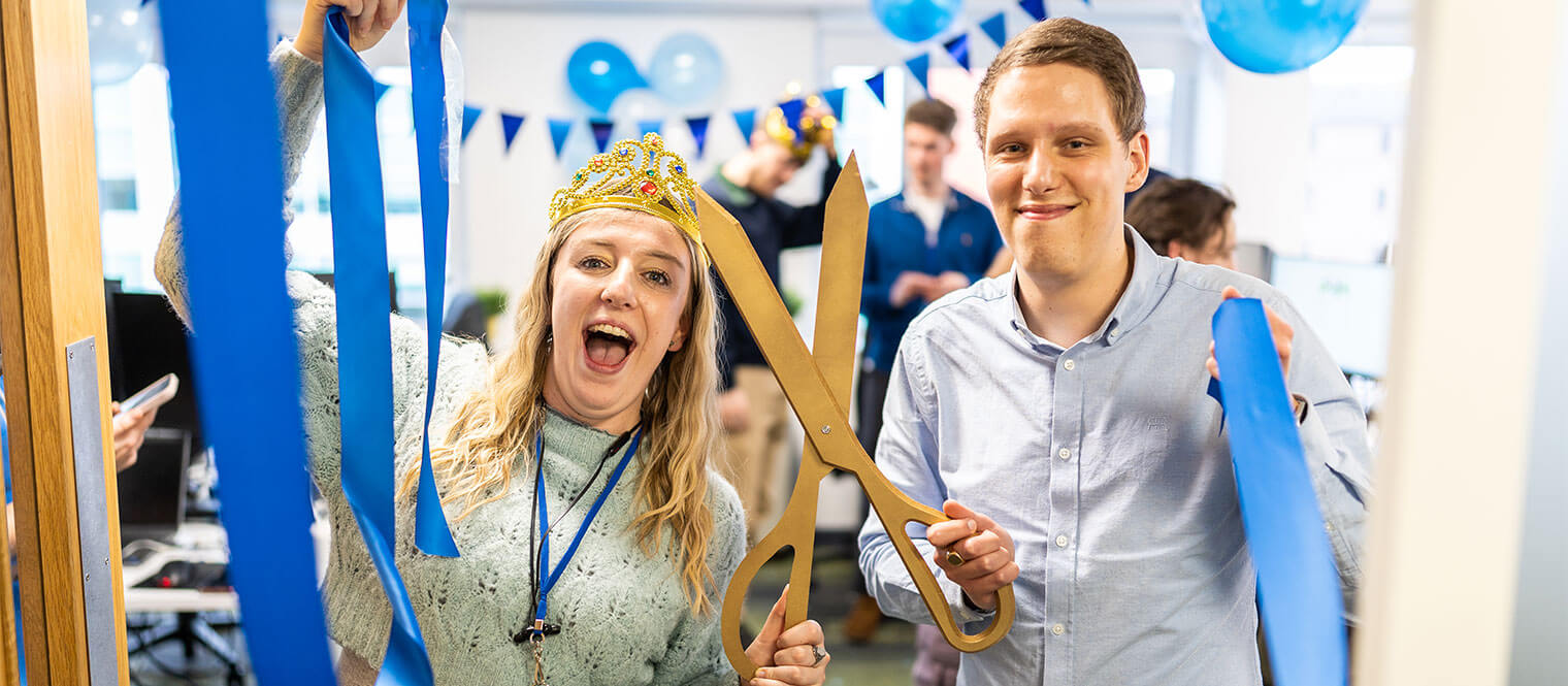 The team celebrating with blue ribbon cutting, bunting and balloons.