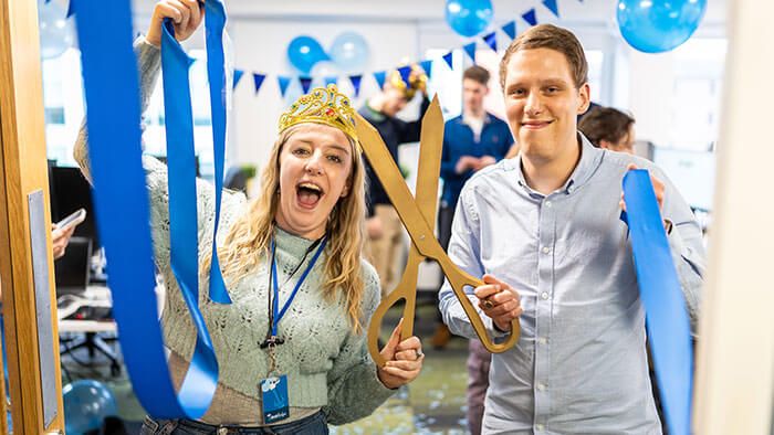 The team celebrating with blue ribbon cutting, bunting and balloons.