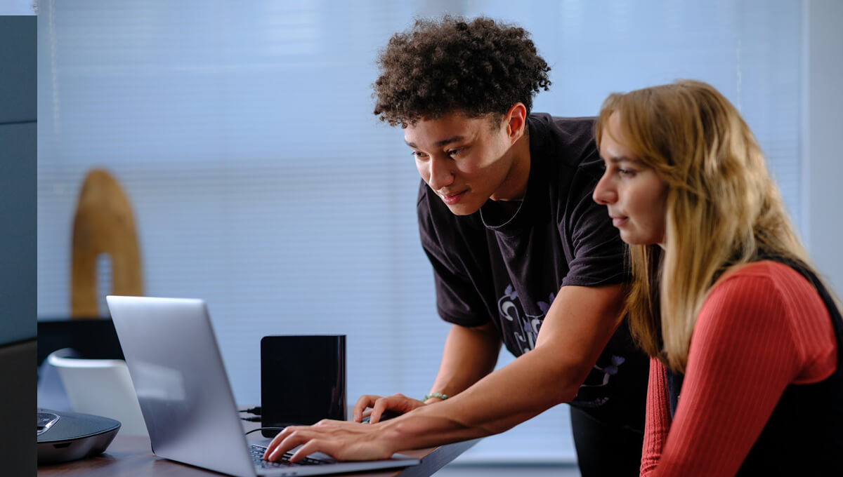 a person assists another colleague by helping them with their laptop