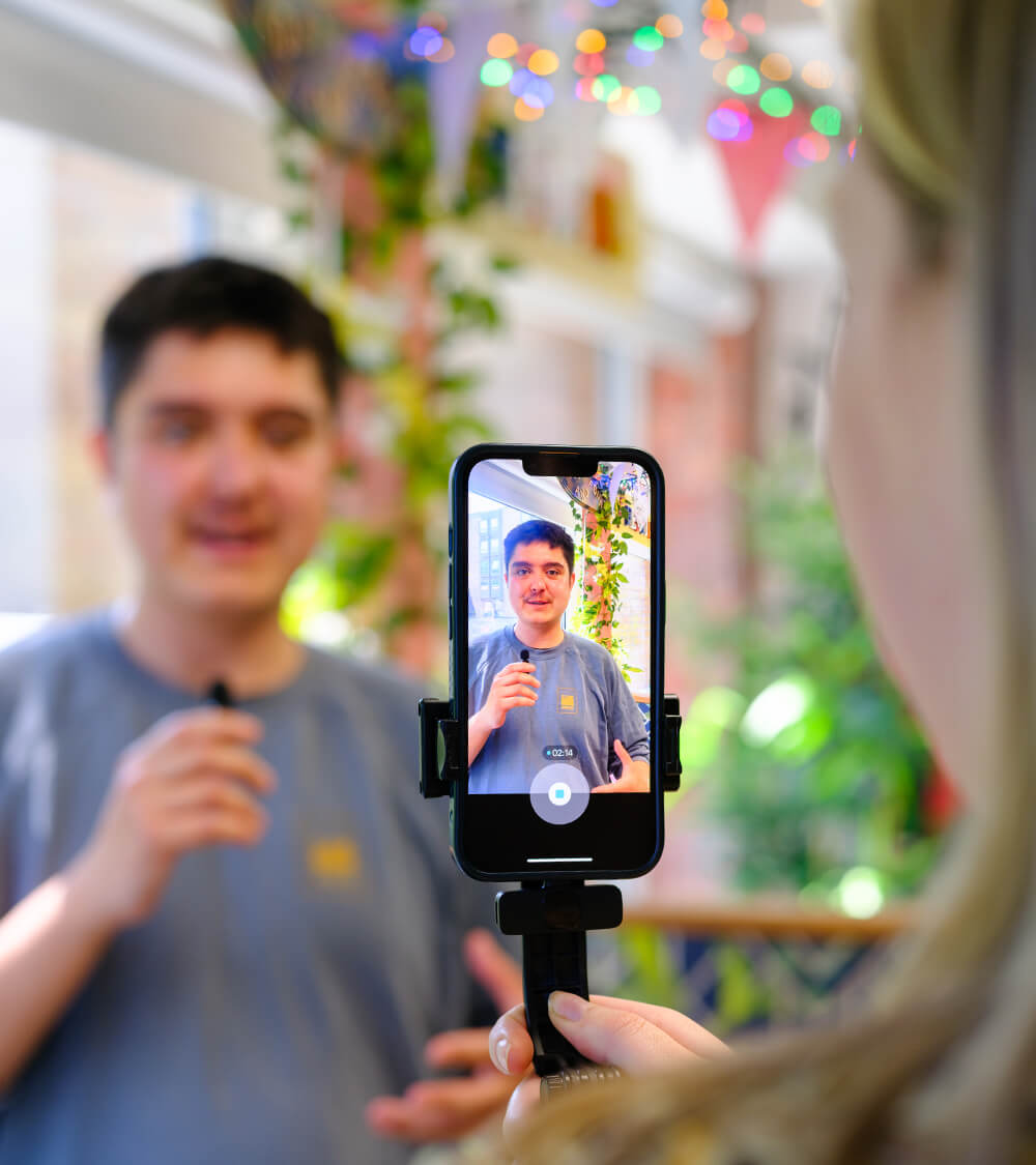 two colleagues film a social media story on their phone in a bright office space