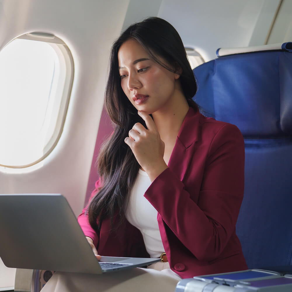 a smartly dressed business woman working on her laptop mid-flight on a commercial passenger aeroplane