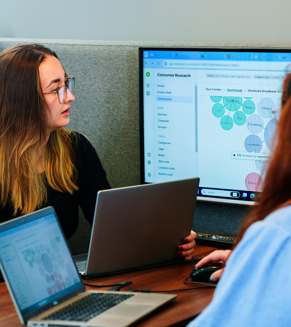 two women sit together in a meeting looking at a screen displaying multiple brand statistics