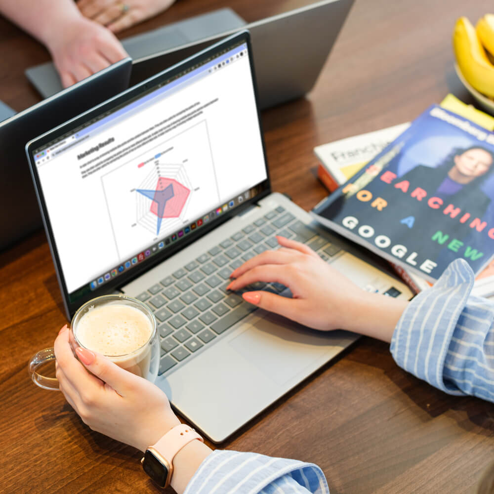 two people sit at a meeting room looking at a laptop showing various data graphs