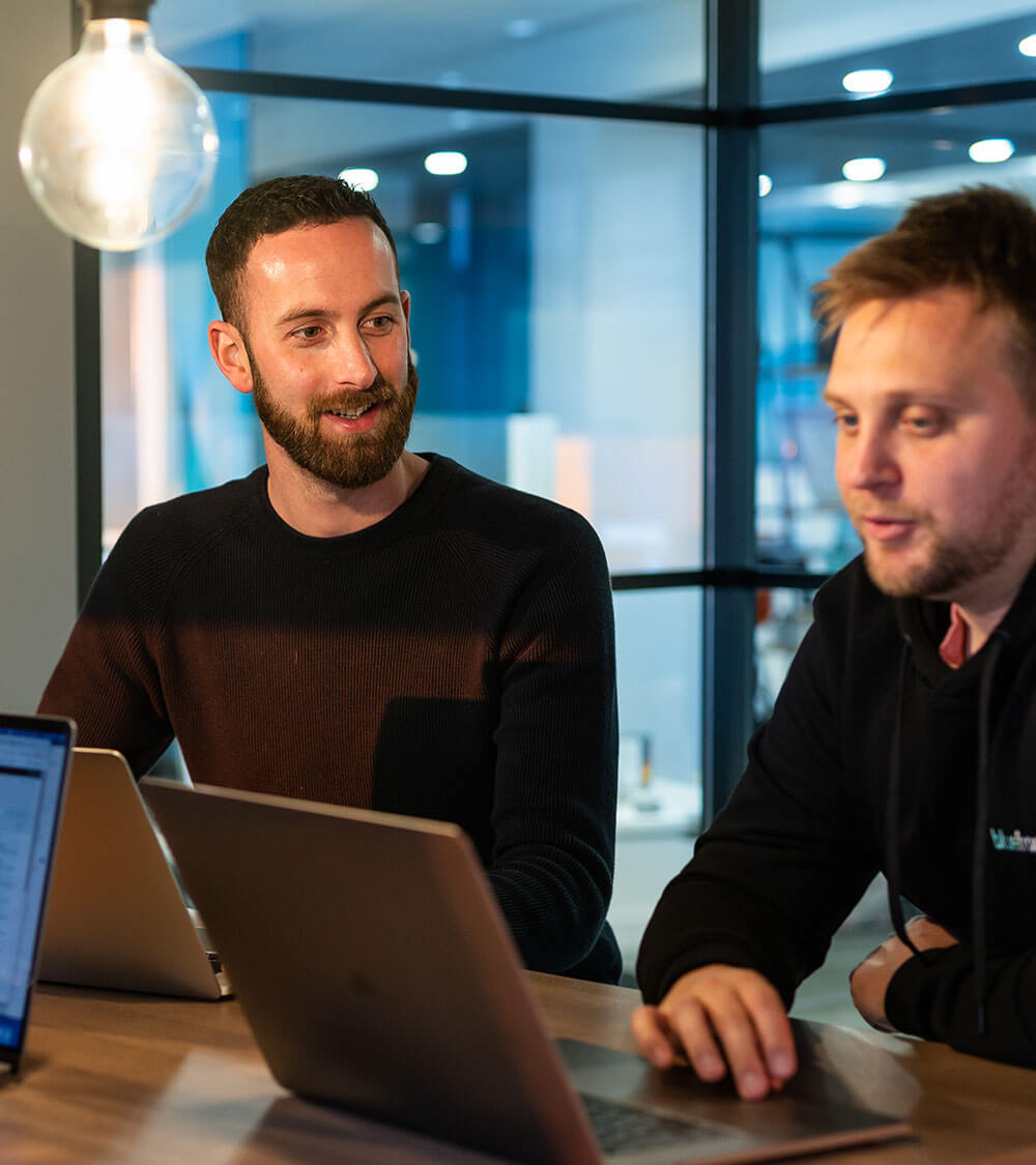 two colleagues sitting together in a meeting space with their laptops