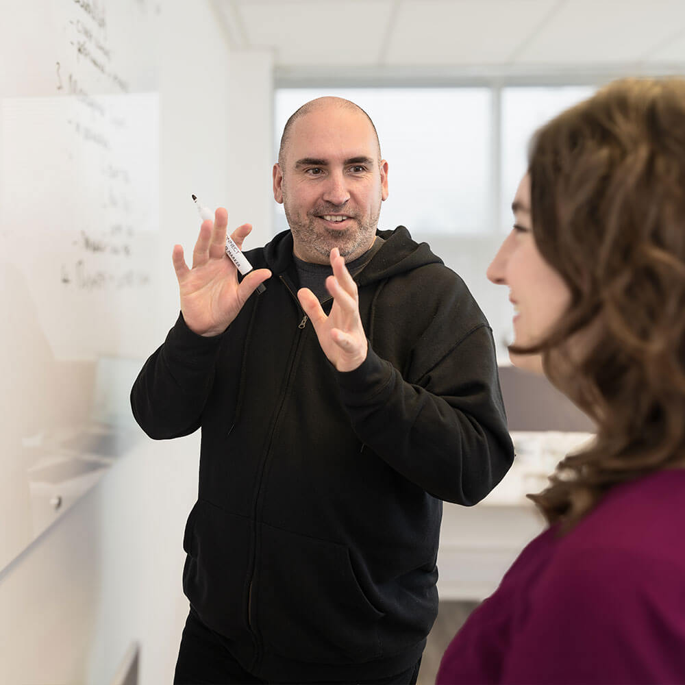 a coworker standing in front of a whiteboard explaining a concept to a client