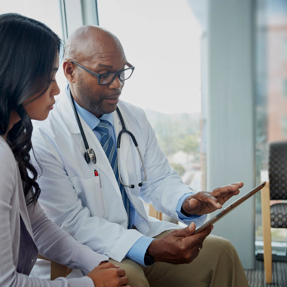 a doctor speaking to a patient and holding a tablet device