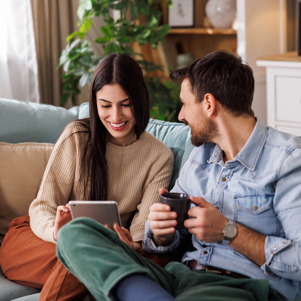 a couple looking at a tablet together on the sofa whilst drinking coffee
