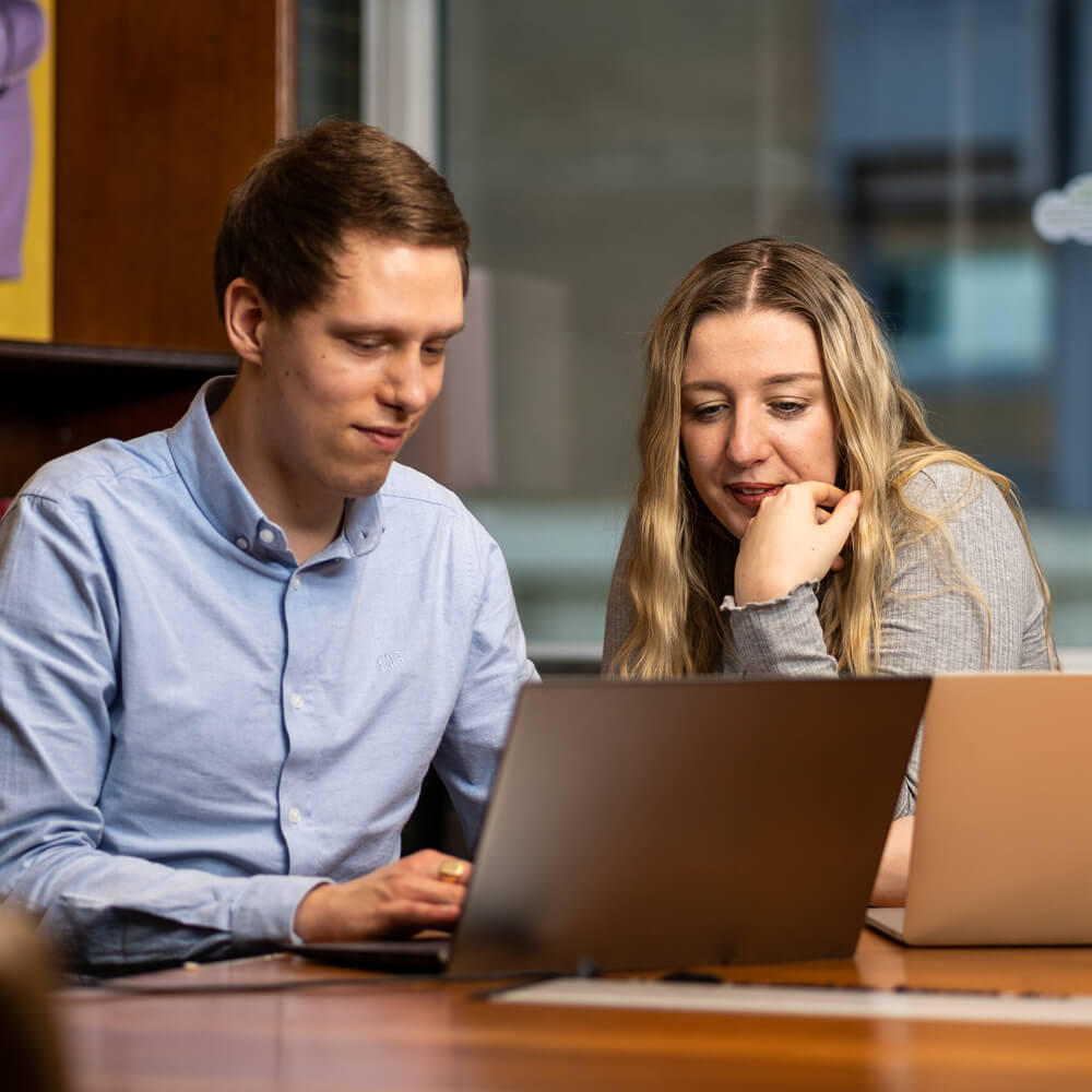 two colleagues work together on a laptop in a sleek meeting room
