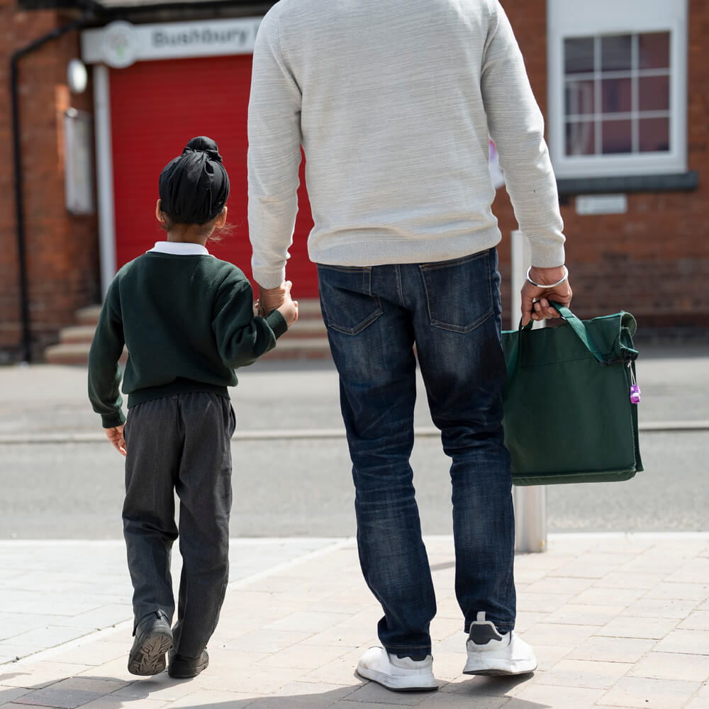 a father walking his son to school carrying a book bag