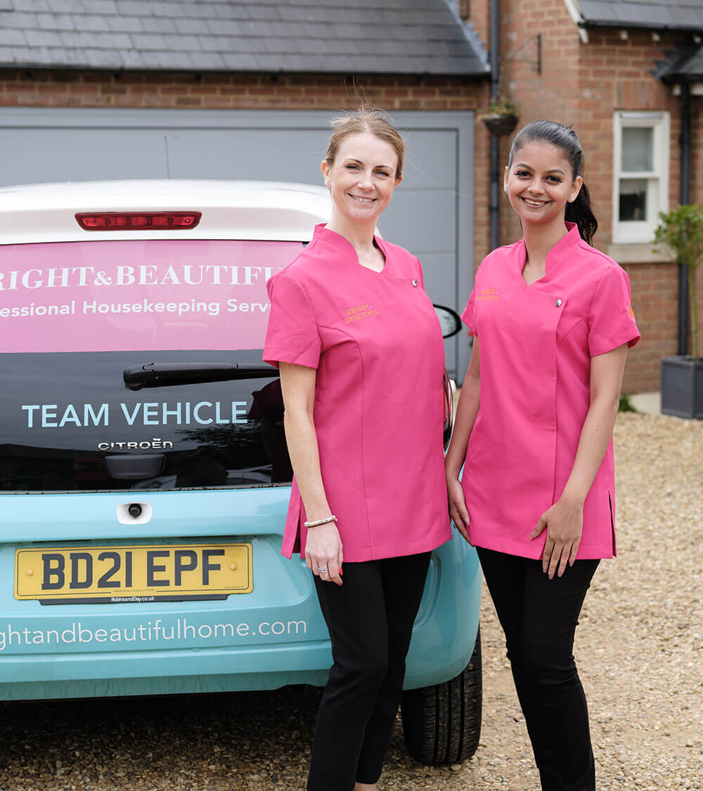 two smartly dressed employees from Bright & Beautiful standing beside a company-branded car