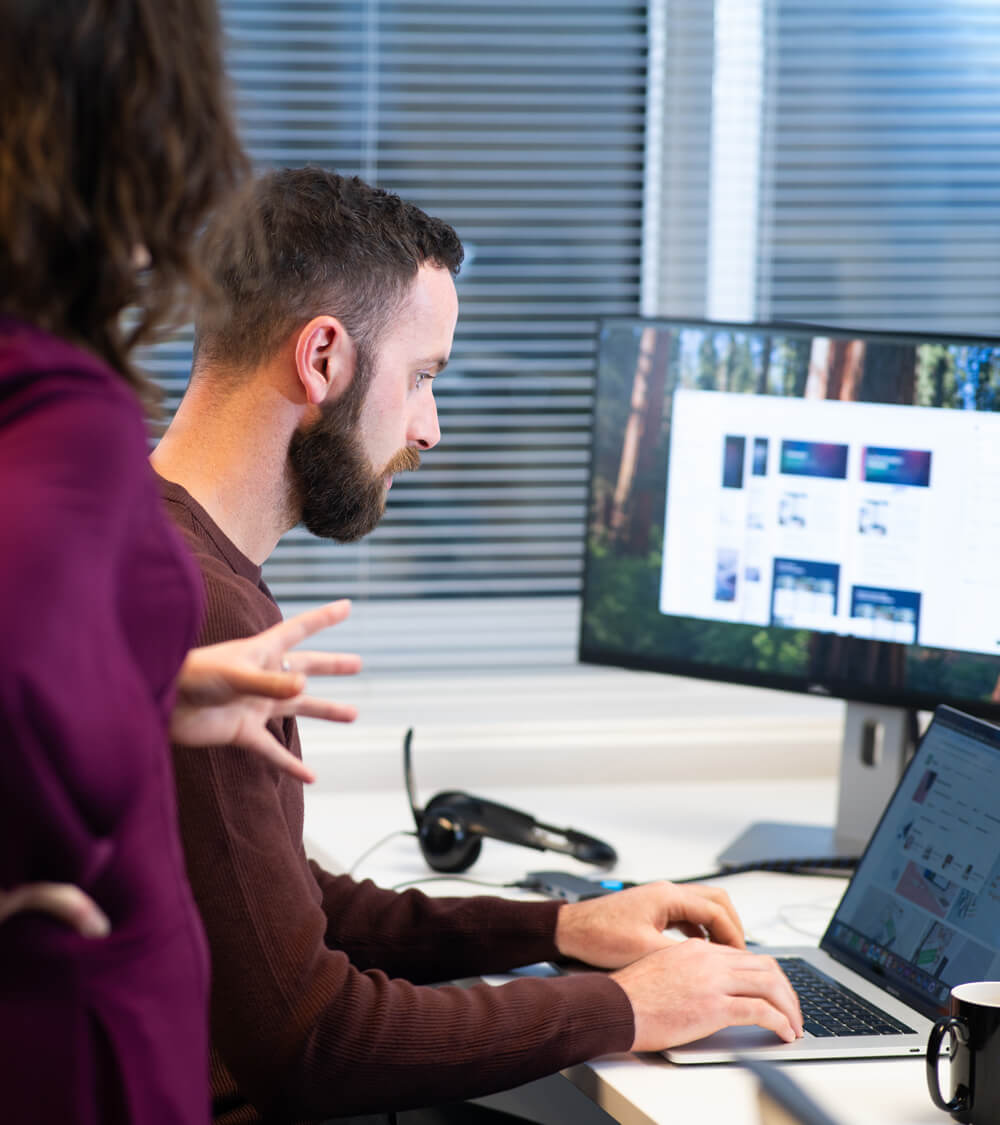 two colleagues looking at a laptop and monitor together