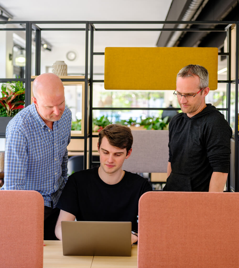 three IT engineers discuss strategy around a laptop
